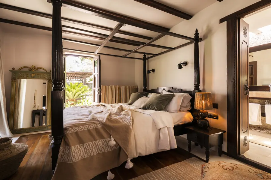 Schlafzimmer mit Himmelbett, offenen Fensterläden ins Grüne und Blick auf ein angrenzendes Bad