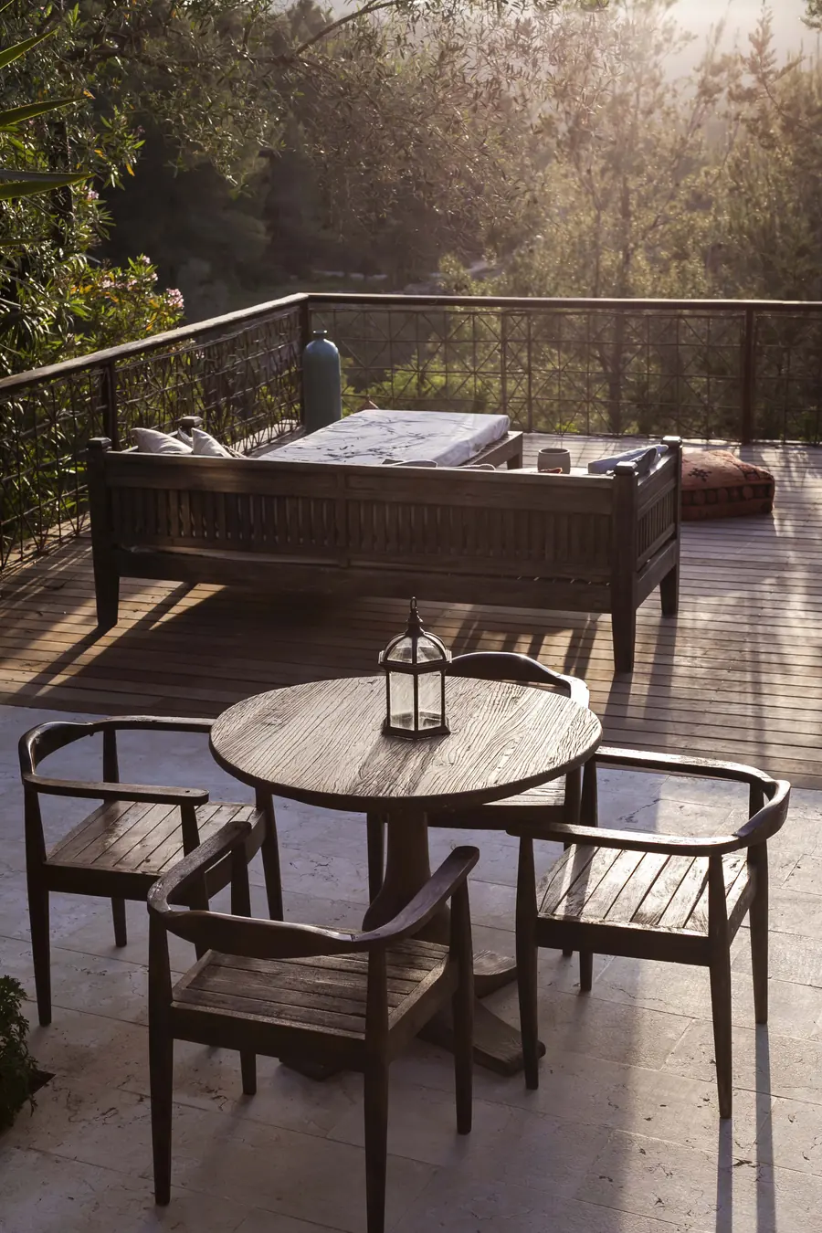 Sonnige Terrasse mit rundem Tisch, Holzstühlen und Tagesbett zwischen Bäumen